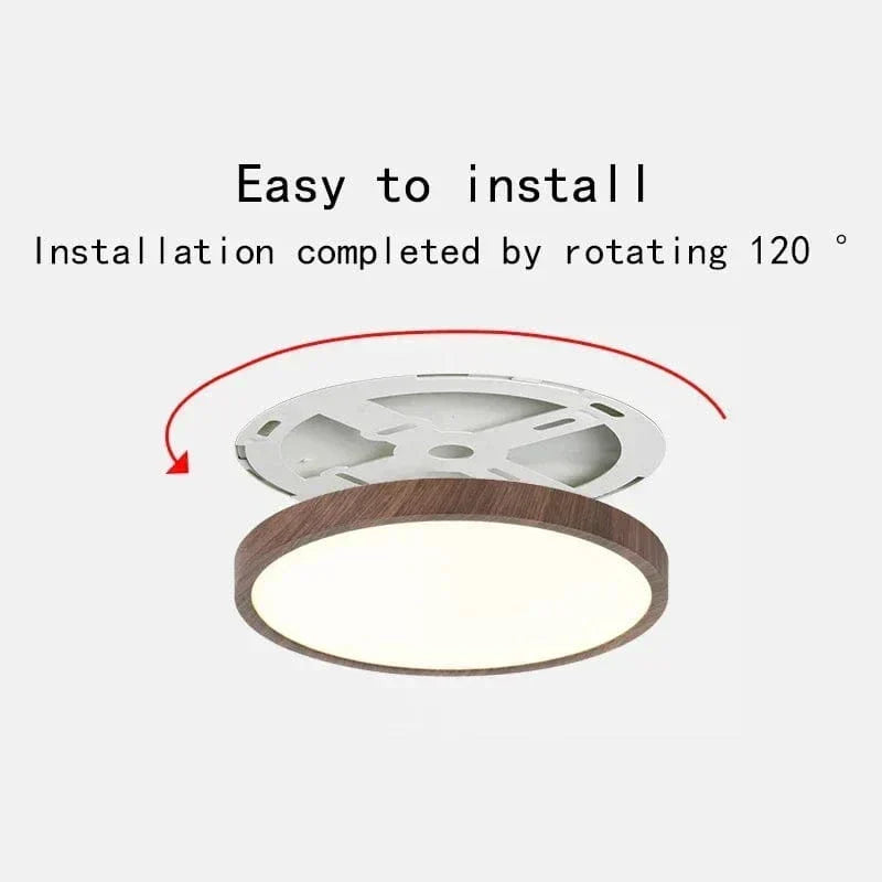 Ronde plafondlamp met donkere houtlook rand en wit montagebeugeltje erboven, met rode pijl die de draaiende montage laat zien. 1