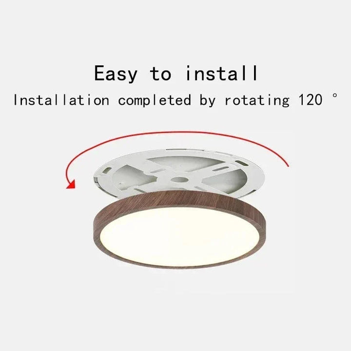 Ronde plafondlamp met donkere houtlook rand en wit montagebeugeltje erboven, met rode pijl die de draaiende montage laat zien. 1