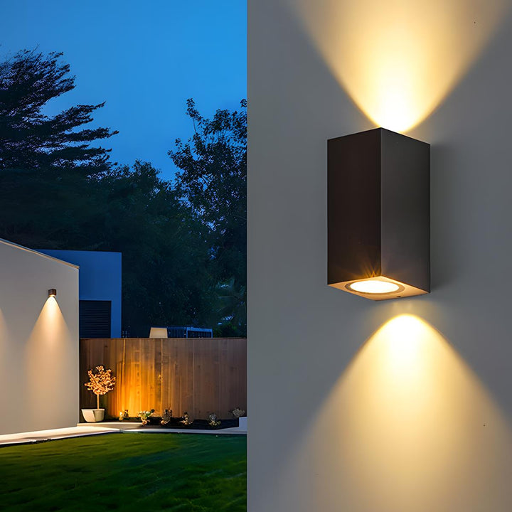 Zwarte langwerpige wandlamp met licht omhoog en omlaag, met een verlichte tuin op de achtergrond 9