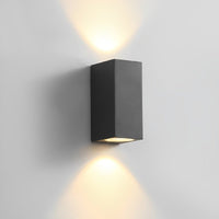 Zwarte dubbele wandlamp van opzij gezien, met warme lichtbundels boven en onder op een lichtgrijze muur 12