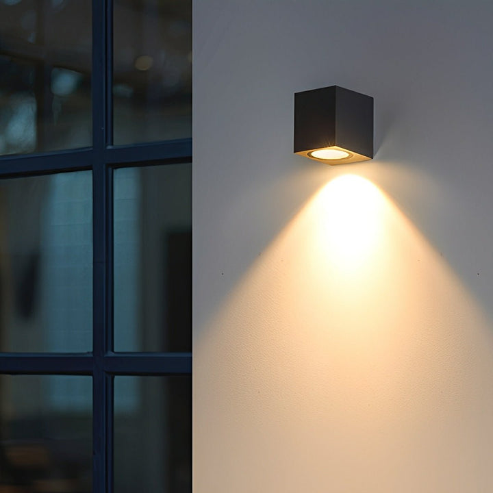 Zwarte kubuslamp met warme neerwaartse lichtkegel op een muur naast een raam met zwarte roedes 11