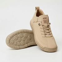 Beige sneaker met veters en elastische band, met een tweede schoen ernaast waarvan de profielzool met ronde noppen zichtbaar is. 1