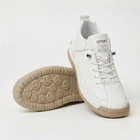 Witte sneaker met elastische veters en beige zool, schuin gezet naast een schoen waarvan de noppenzool naar boven wijst. 2
