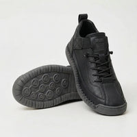 Zwarte sneaker met korrelig oppervlak en donkergrijze zool, met de ronde noppenzool van de tweede schoen in beeld. 3
