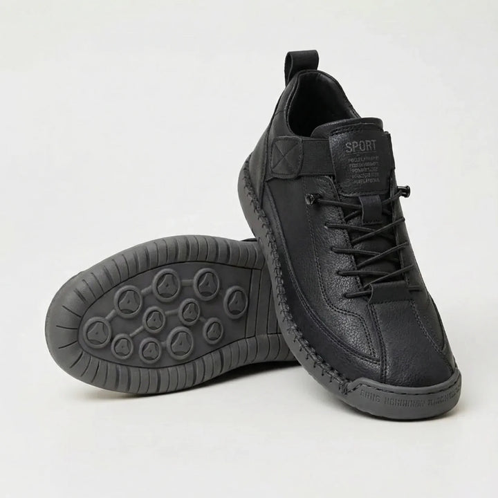 Zwarte sneaker met korrelig oppervlak en donkergrijze zool, met de ronde noppenzool van de tweede schoen in beeld. 3