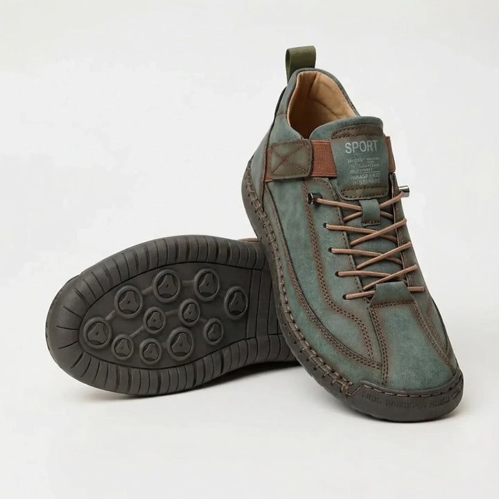 Groene sneaker met bruine elastische veters en bandje, met de donkere noppenzool van de andere schoen zichtbaar. 5