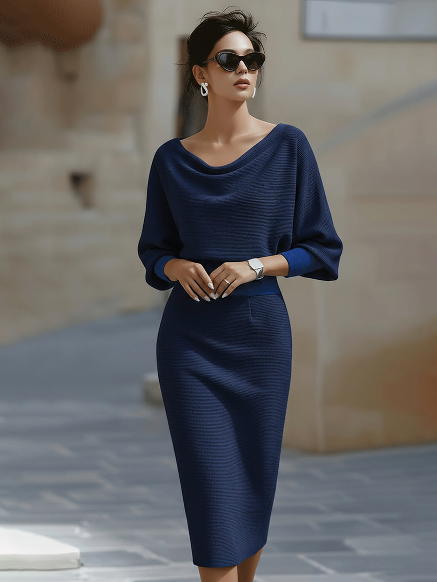 Model met zonnebril draagt de jurk in marineblauw, vooraanzicht met gedrapeerde hals en wijde mouwen met helderblauwe manchetten. 6