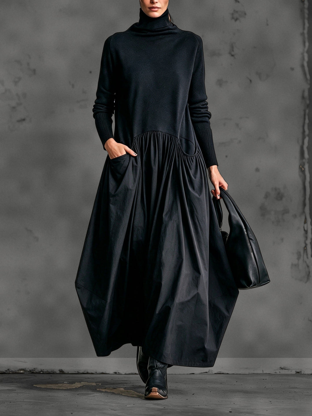 Model in zwarte maxi-jurk met opstaande kraag, hand in de zak, zwarte tas en laarzen 1