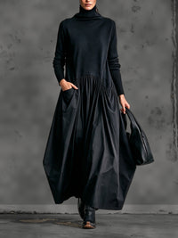 Model in zwarte maxi-jurk met opstaande kraag, hand in de zak, zwarte tas en laarzen 1