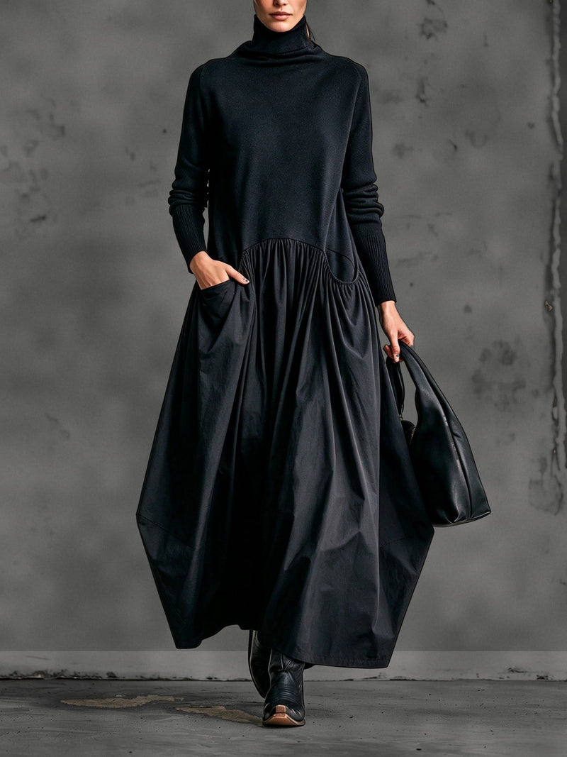 Model in zwarte maxi-jurk met opstaande kraag, hand in de zak, zwarte tas en laarzen 1