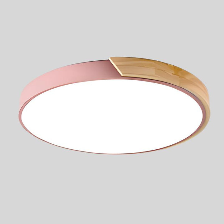 Roze ronde plafondlamp met houten accent langs een deel van de rand, los afgebeeld op lichtgrijze achtergrond. 16