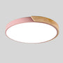 Roze ronde plafondlamp met houten accent langs een deel van de rand, los afgebeeld op lichtgrijze achtergrond. 16