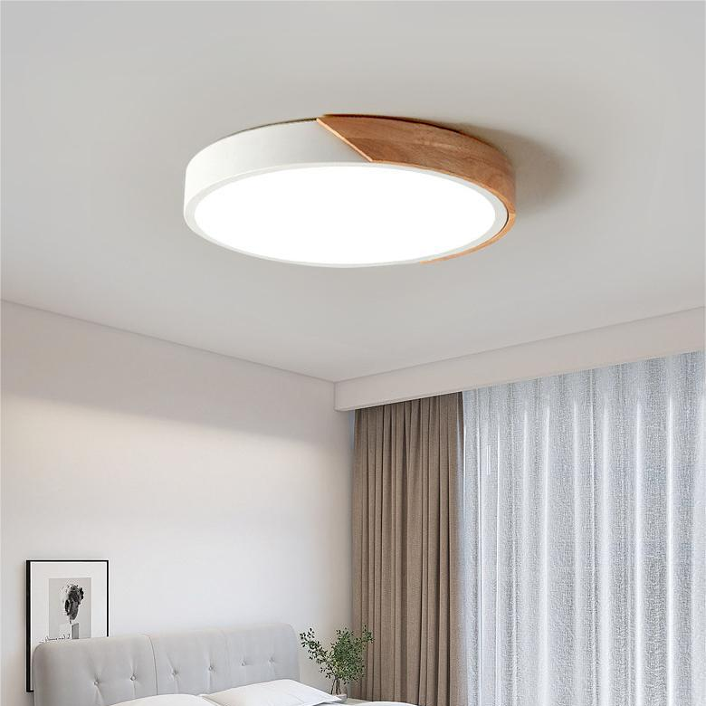 Witte ronde plafondlamp met houten accent aan de rand, brandend in een slaapkamer met gordijnen en een bed. 3