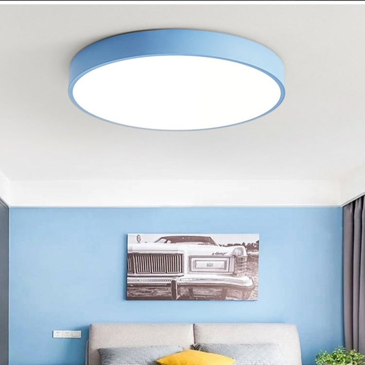 Blauwe ronde plafondlamp zonder houtaccent, brandend boven een slaapkamer met blauwe muur en een zwart-wit kunstwerk. 4