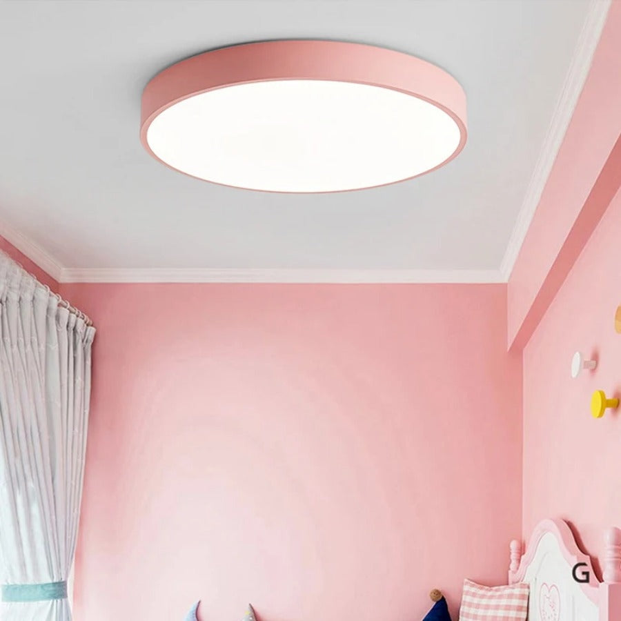 Roze ronde plafondlamp zonder houtaccent, brandend in een roze kinderkamer met gordijn en kapstokhaakjes. 5