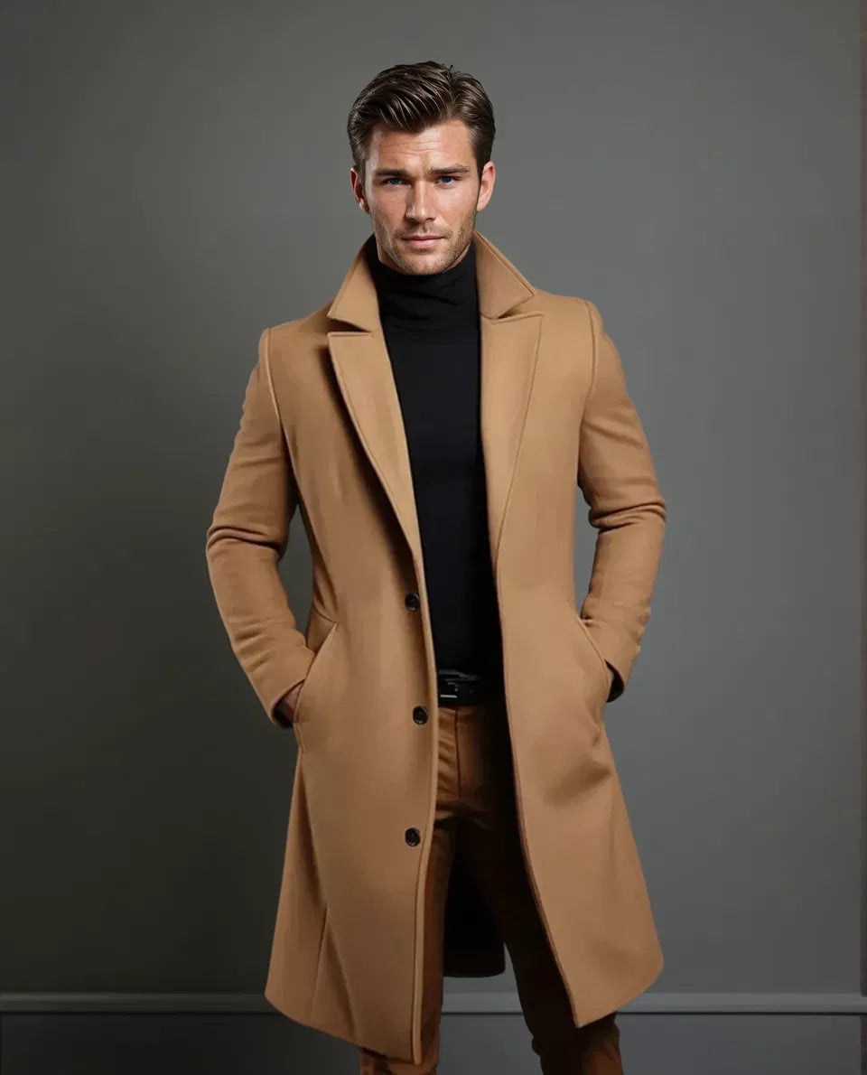 Ruimer beeld van het model in de kameelkleurige overjas met brede revers, zwarte coltrui en bruine broek, bijna ten voeten uit. 5