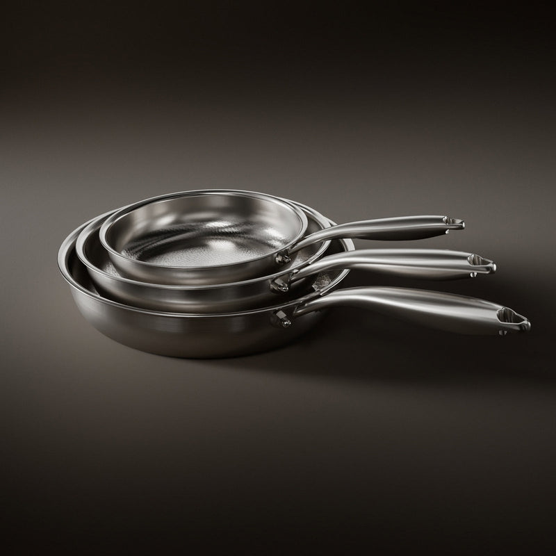 Drie in elkaar gestapelde koekenpannen van verschillende grootte met geborstelde stalen handvatten op een donkere 1
