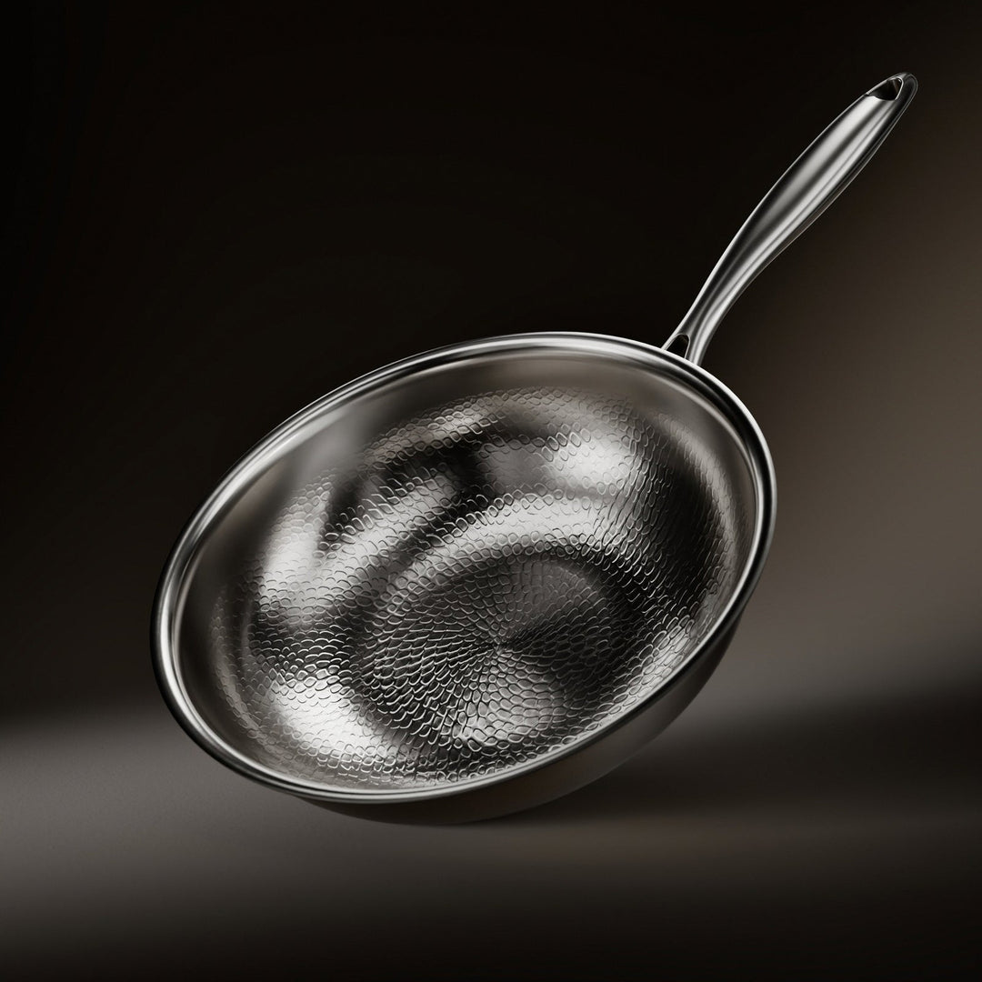 Schuin van boven gezien: de wokpan met het gehamerde schubbenpatroon in de binnenkant, de glanzende rand en de metalen steel op donkere achtergrond. 1