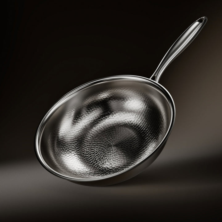 Schuin van boven gezien: de wokpan met het gehamerde schubbenpatroon in de binnenkant, de glanzende rand en de metalen steel op donkere achtergrond. 1