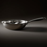 Zijaanzicht van de wokpan met gladde, gebogen buitenkant en lange metalen steel, met het gehamerde oppervlak aan de binnenkant zichtbaar. 2