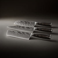 De drie messen naast elkaar liggend van boven naar beneden, met een santoku met kuiltjes, een koksmes en een hakmes. 2