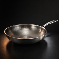 Lege wokpan met gehamerd patroon aan de binnenkant en metalen steel, schuin van opzij gefotografeerd op een donkere ondergrond. 1