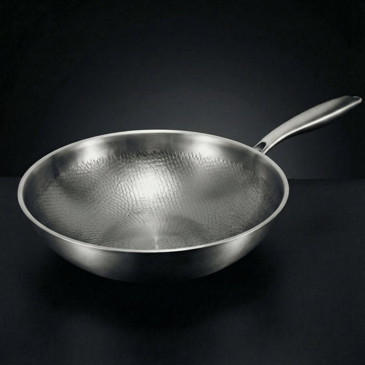 Lege wokpan met gehamerd oppervlak en lange metalen steel, schuin van boven gezien tegen een donkere achtergrond. 1