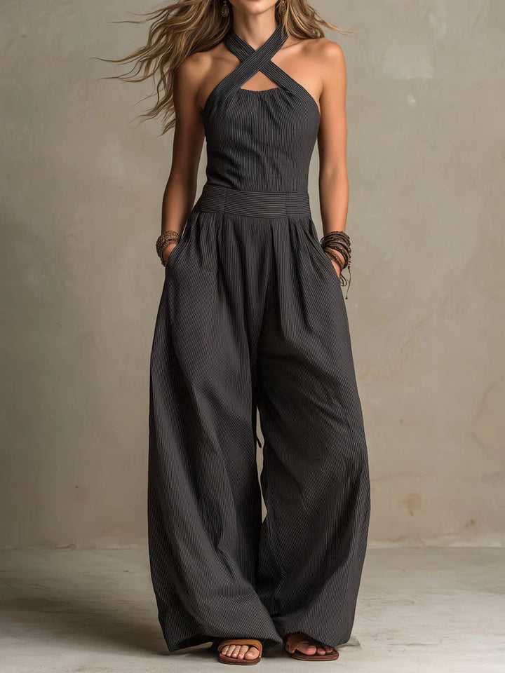 Model draagt de jumpsuit in donkergrijs met fijn streepje, overslaghalslijn, handen in de zakken en bruine sandalen. 1