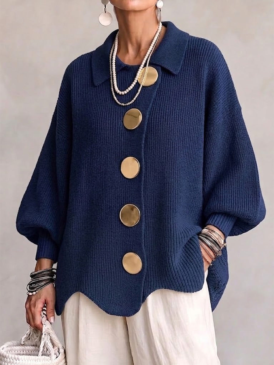 Model draagt het gebreide vest in marineblauw met gouden knopen, parelkettingen en een witte linnen broek, vooraanzicht. 1