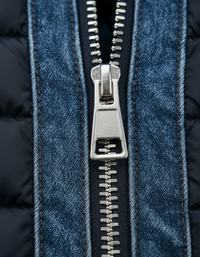Detail van de metalen ritssluiting met trekker, omlijst door gestikte denim banden en donkerblauwe gewatteerde stof. 4