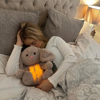 Vrouw met blond haar ligt slapend in bed en houdt een konijn met oplichtende buik stevig vast. 16
