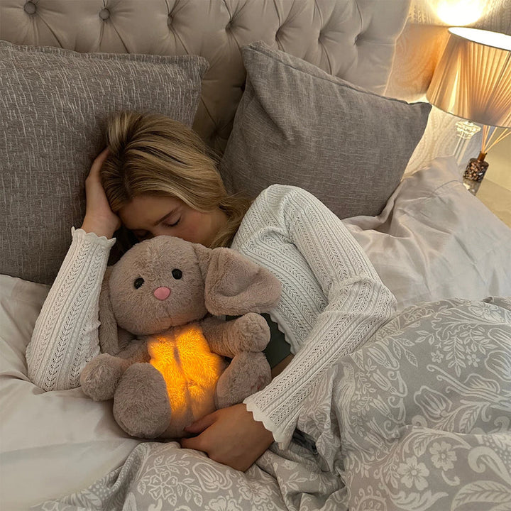 Vrouw met blond haar ligt slapend in bed en houdt een konijn met oplichtende buik stevig vast. 16