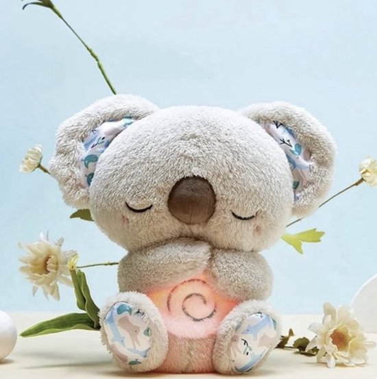 Koalaknuffel met gesloten ogen en gevouwen pootjes, een zachtroze spiraal op de buik, tussen witte bloemen tegen een lichtblauwe achtergrond. 1
