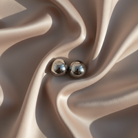 Twee glanzende zilverkleurige metalen bolletjes naast elkaar op plooiend beige satijn, met spiegelende reflecties in het metaal. 1