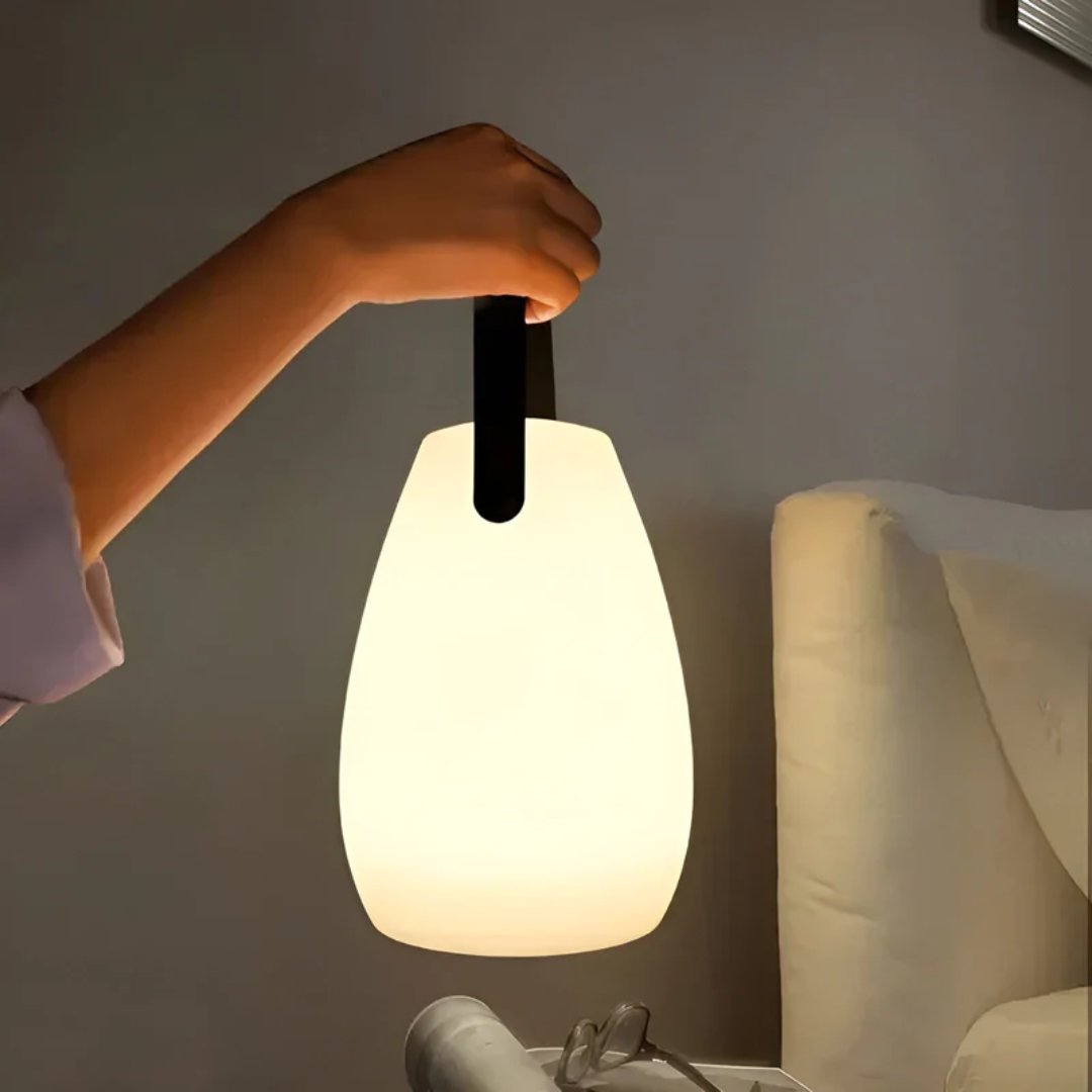 Hand houdt de druppelvormige lamp aan de zwarte lus omhoog naast een bed met bril 1