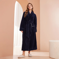 Model in marineblauwe badjas met sjaalkraag en ceintuur, in een roze kamer met boog 1