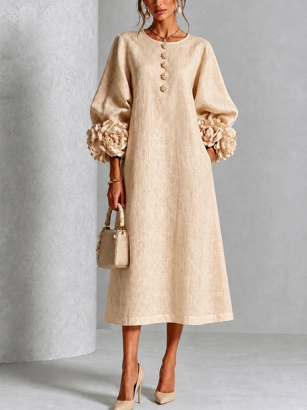Vooraanzicht van de jurk in zandbeige op een model, met bloemenknopen aan de hals, ruime mouwen en rozen aan de manchetten. 4