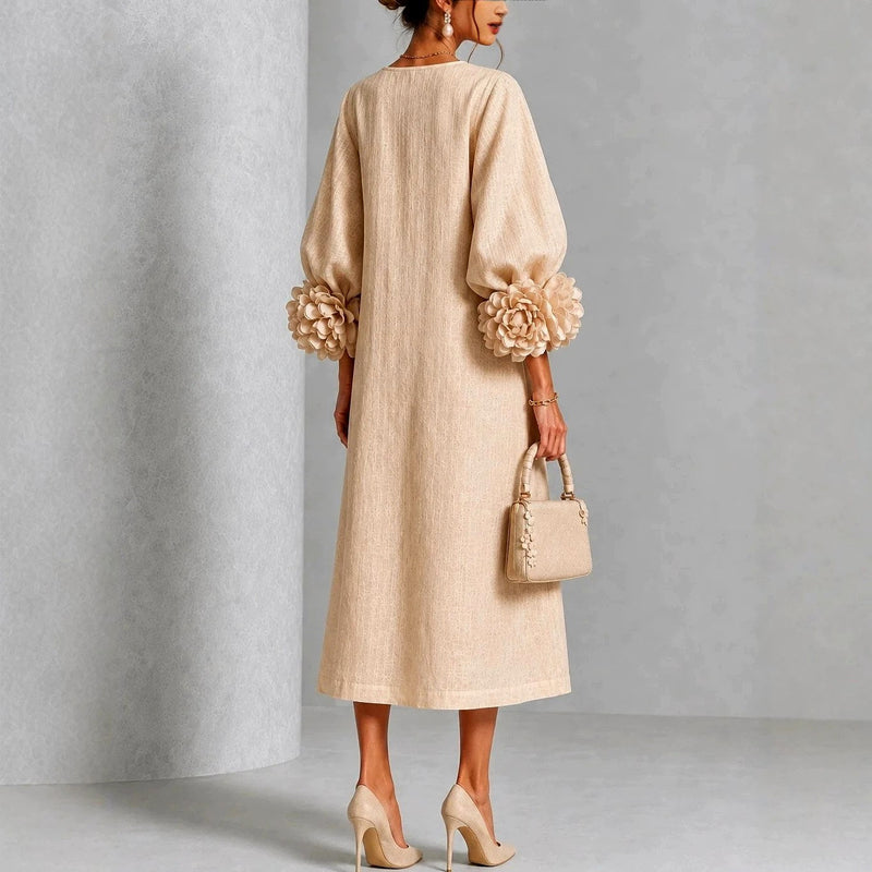 Achteraanzicht van de beige jurk op een model: gesloten rug, A-lijn zoom en grote stoffen rozen aan de mouwuiteinden. 5