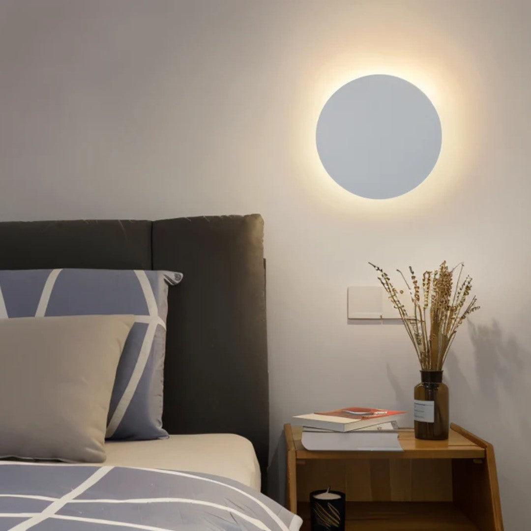 Witte ronde wandlamp naast een bed, boven een houten nachtkastje met boeken en droogbloemen 7