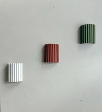 Witte, terracotta en groene geribbelde wandlamp schuin onder elkaar tegen een grijze muur gemonteerd 12