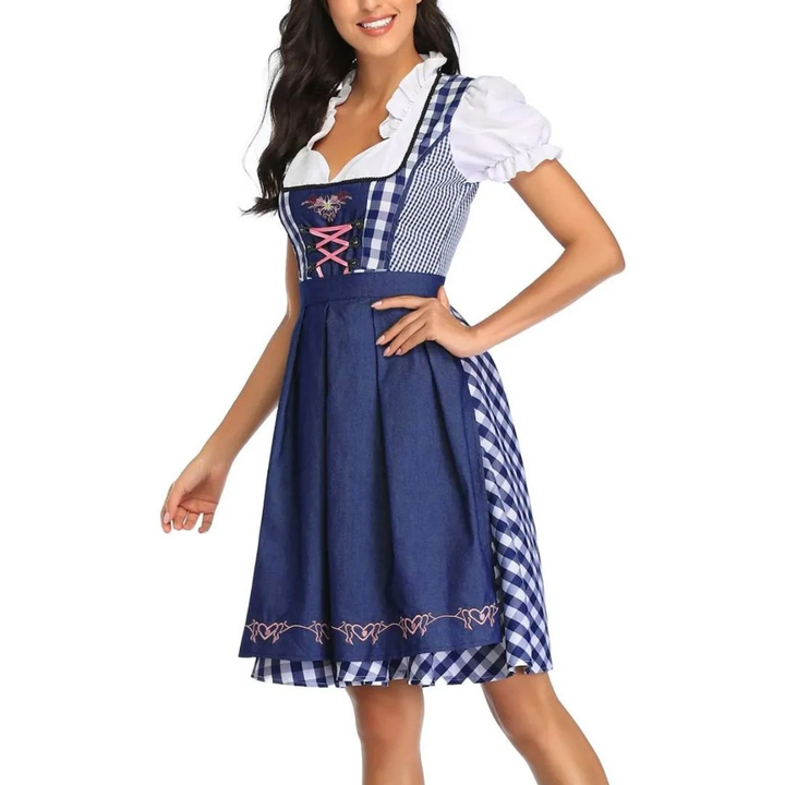 Model met hand op de heup in de blauw-wit geruite dirndl met donkerblauwe schort, roze veters en witte pofmouwen, schuin vooraanzicht. 6