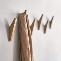 Rij houten haken aan een witte muur, waarvan een haak een beige sjaal draagt. 2