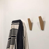 Twee houten haken aan een witte muur naast een zwart-wit gestreepte handdoek die aan een haak hangt. 4