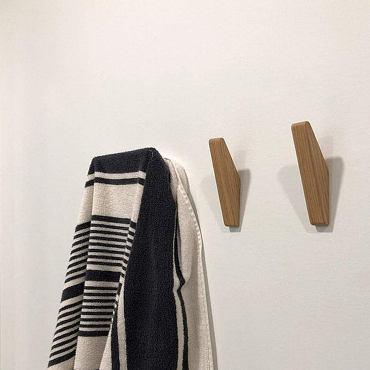 Twee houten haken aan een witte muur naast een zwart-wit gestreepte handdoek die aan een haak hangt. 4