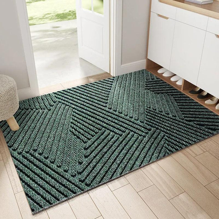 Groene deurmat met geometrisch ribbelpatroon bij een open voordeur, naast een schoenenkast in een hal 1
