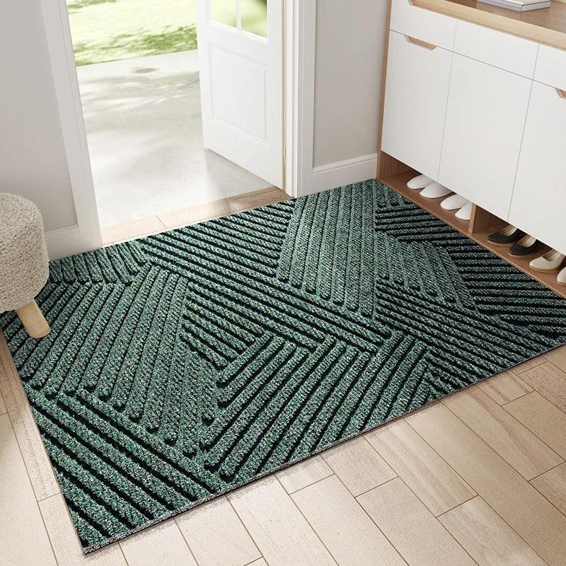 Groene deurmat met reliëfpatroon van diagonale en driehoekige ribbels, gelegd in een lichte hal bij de openstaande voordeur. 1