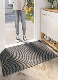 Grijs gestreepte deurmat met gebogen ribbels voor de open voordeur, met een persoon in spijkerbroek en sneakers op de drempel. 5