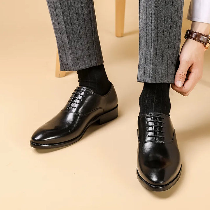 Zwarte glanzende veterschoenen gedragen met grijze krijtstreepbroek en zwarte sokken, een hand trekt de broekspijp omhoog 1