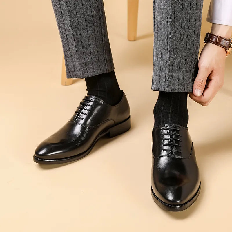Zwarte glanzende veterschoenen gedragen met grijze krijtstreepbroek en zwarte sokken, een hand trekt de broekspijp omhoog 1