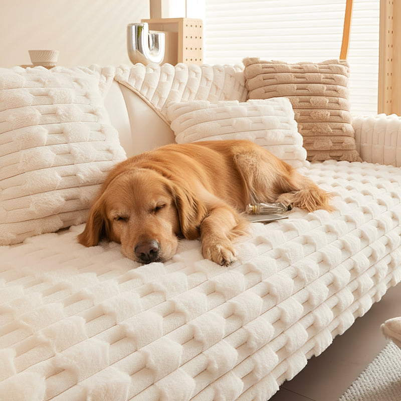 Golden retriever slaapt op een crèmewitte pluche bankhoes met reliëfpatroon, tussen bijpassende kussens op de bank. 1